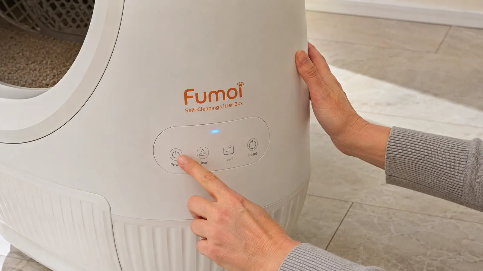 Person setting up the Fumoi automatic self-cleaning litter box, pressing the power button on the side panel