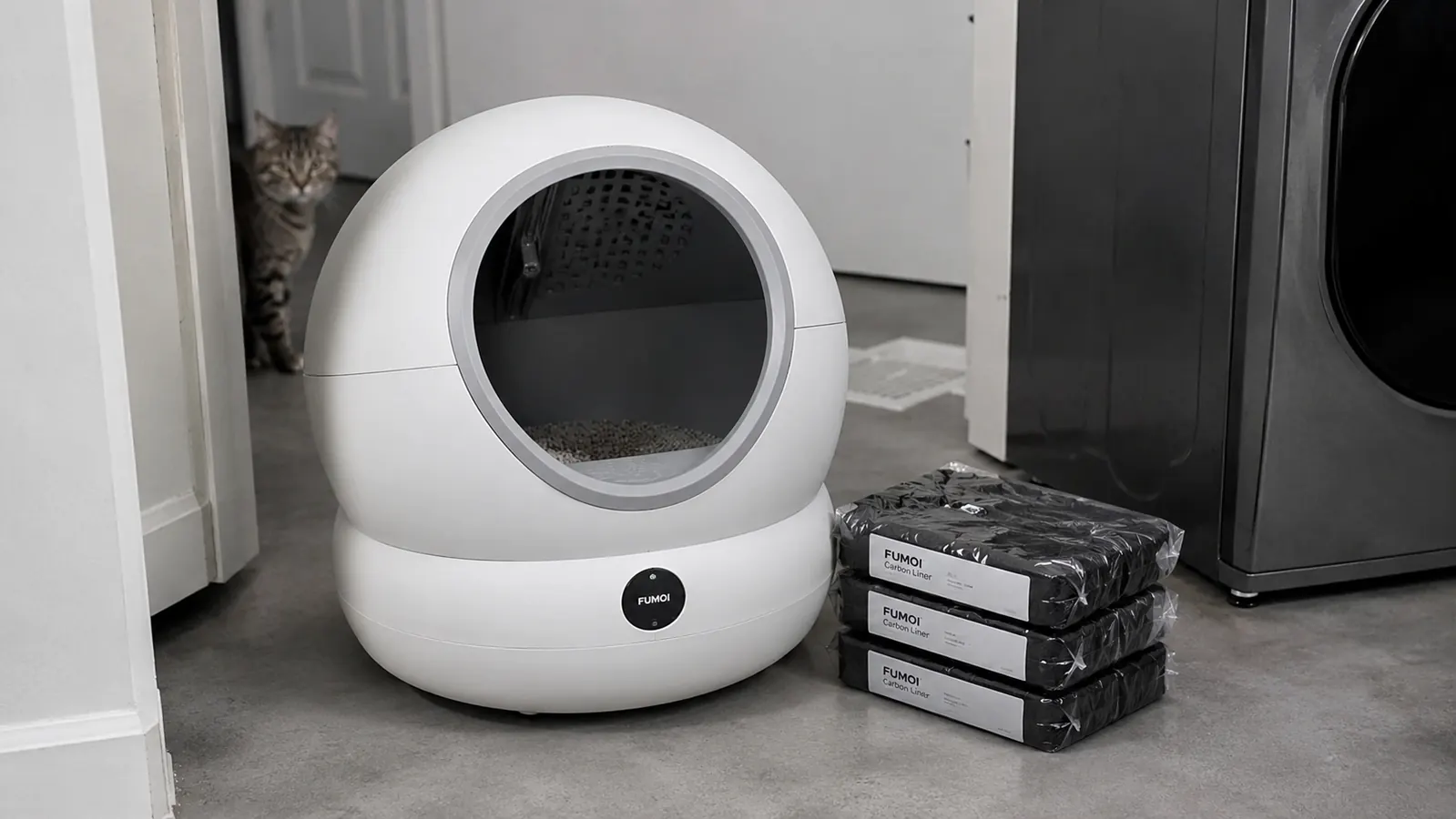 Fumoi self-cleaning litter box globe sitting on a gray utility room floor beside a small stack of carbon liner bags